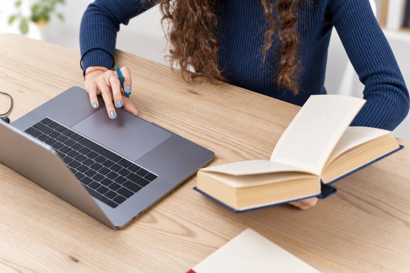 Une personne travaille sur un ordinateur portable avec un livre ouvert